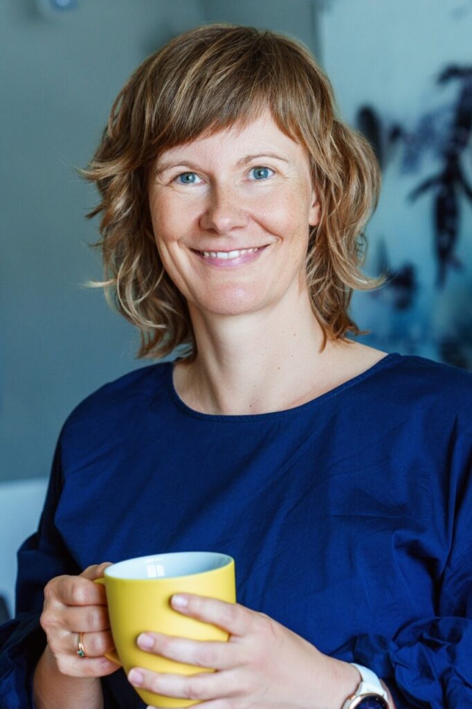 Foto einer blonden Frau mit blauem Pulli und gelber Tasse in der Hand