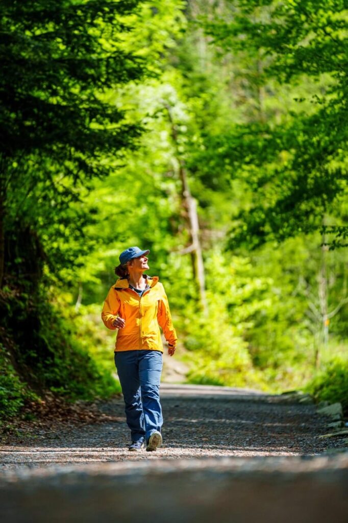 Frau mit gelber Jacke läuft auf einem Waldweg